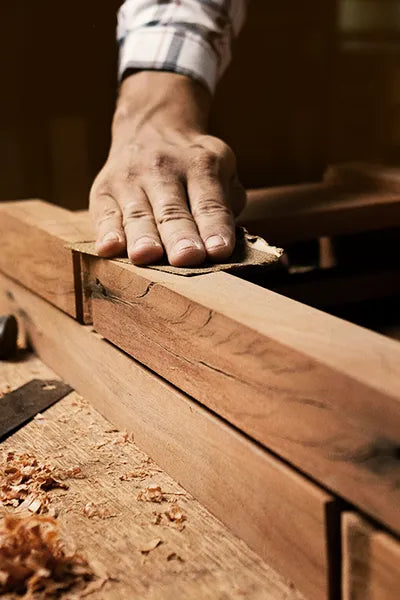 Hand using a sanding block on a wooden surface with wood shavings around