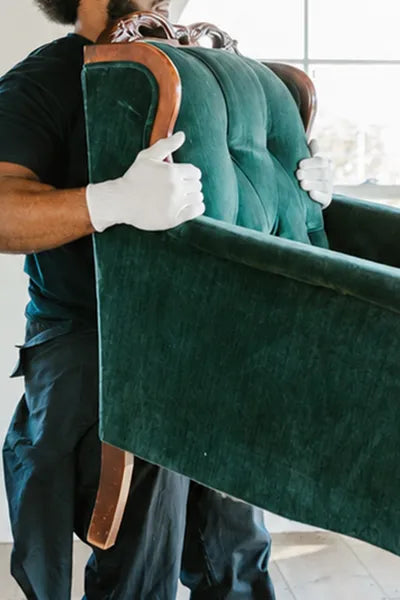 Person carrying a green upholstered chair with white gloves