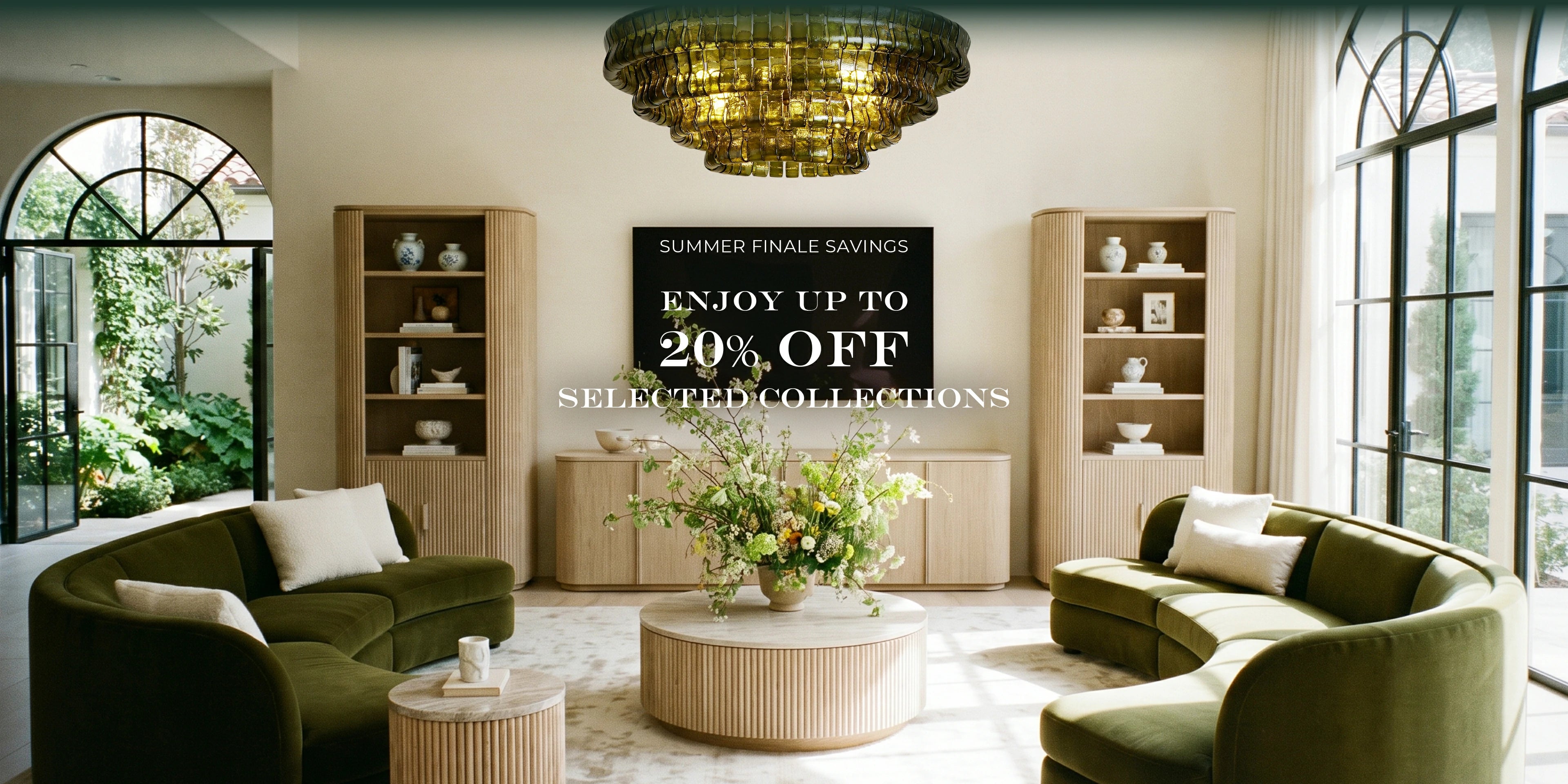 A luxury interior showroom with two curved olive green sofas, light wood shelving, a chandelier, and a central promotional sign reading 'Summer Finale Savings. Enjoy up to 20% off selected collections.
